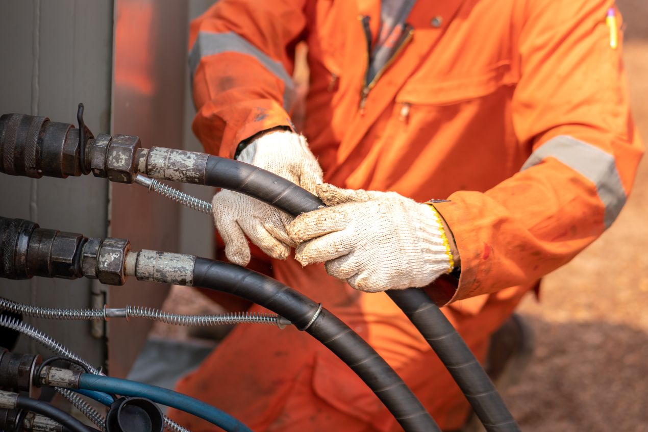 Industriemitarbeiter mit Schutzhandschuhen haelt zwei dicke Industrieschlaeuche in Arbeitsumgebung